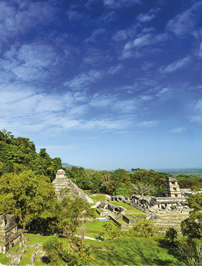 A wide view of Palenque featuring the main palace and several temples against a beautiful blue sky