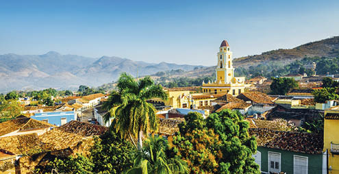 Panoramic view over the city of Trinidad, Cuba with mountains in the background and a blue sky. The bell tower belongs to the Iglesia y Convento de San Francisco.