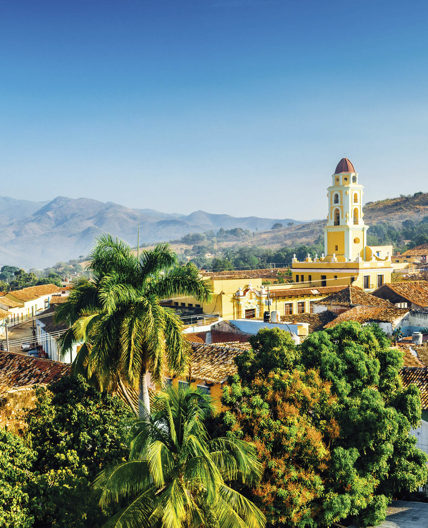 Panoramic view over the city of Trinidad, Cuba with mountains in the background and a blue sky. The bell tower belongs to the Iglesia y Convento de San Francisco.
